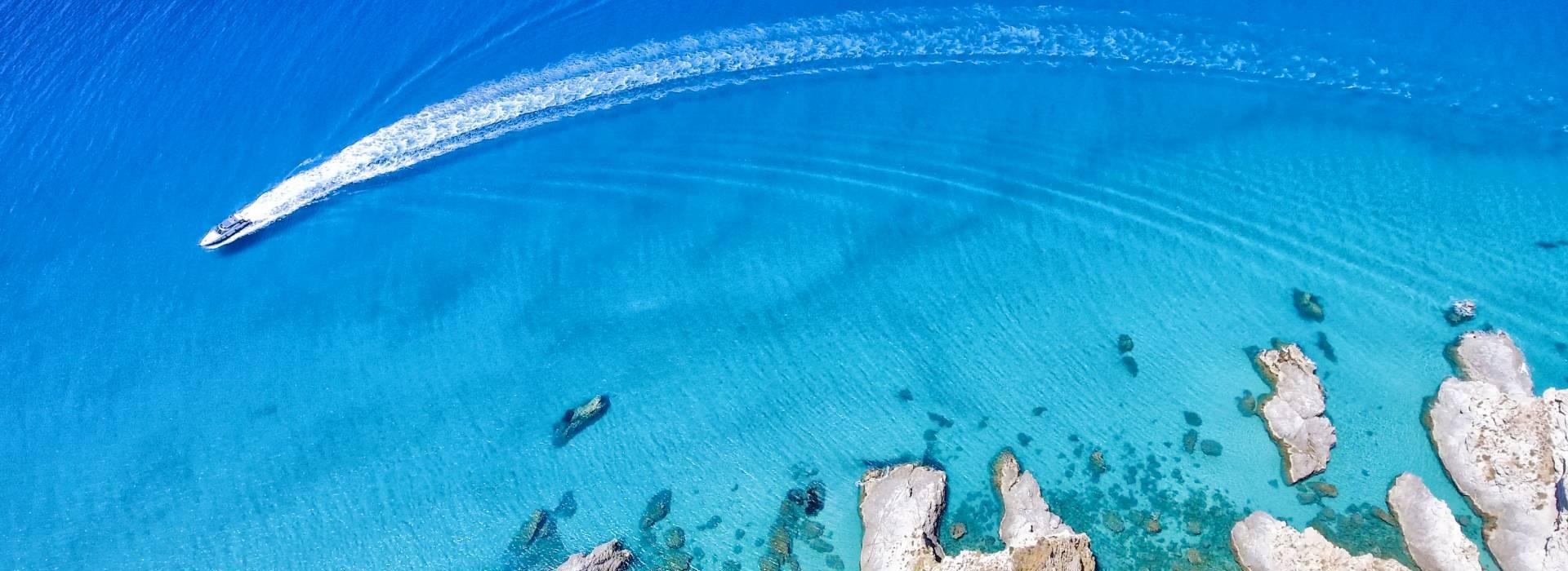 Mare cristallino con barca che lascia una scia, rocce visibili sott'acqua.