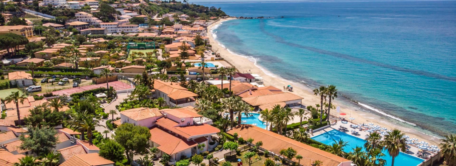 Vista aerea di un resort con piscina, spiaggia e mare cristallino.