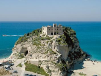 Isola rocciosa con chiesa storica, circondata da spiagge e mare blu.