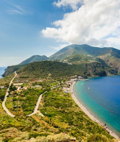 Spiaggia e paesaggio collinare con mare azzurro e vegetazione rigogliosa.