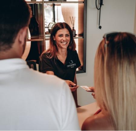 Receptionist sorridente accoglie clienti al banco di un hotel.