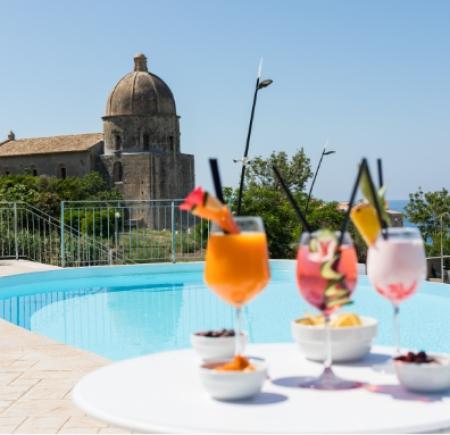 Cocktail a bordo piscina con vista su un'antica chiesa e il mare.