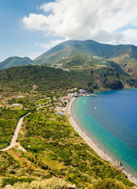 Spiaggia con mare cristallino e colline verdi, paesaggio mediterraneo.