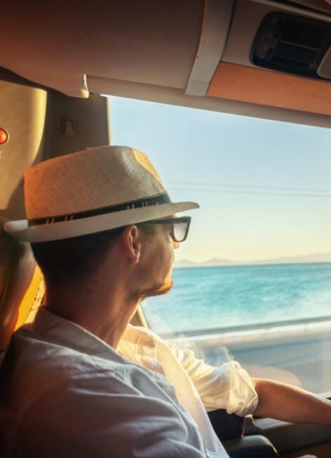 Uomo con cappello guarda il mare dal finestrino di un'auto al tramonto.