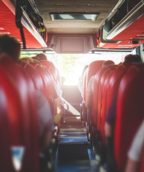 Interno di un autobus con sedili rossi e passeggeri seduti.