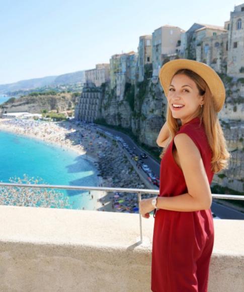 Donna sorridente con cappello, vista mare e scogliere in una giornata soleggiata.