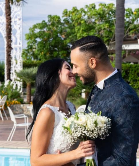 Coppia felice si sposa all'aperto, vicino a una piscina, con fiori bianchi.