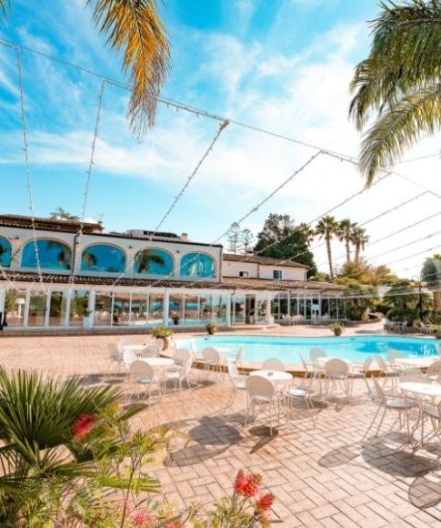 Piscina all'aperto con sedie bianche, palme e cielo sereno in un resort.