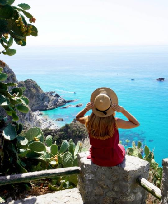 Donna con cappello ammira il mare azzurro da un punto panoramico.