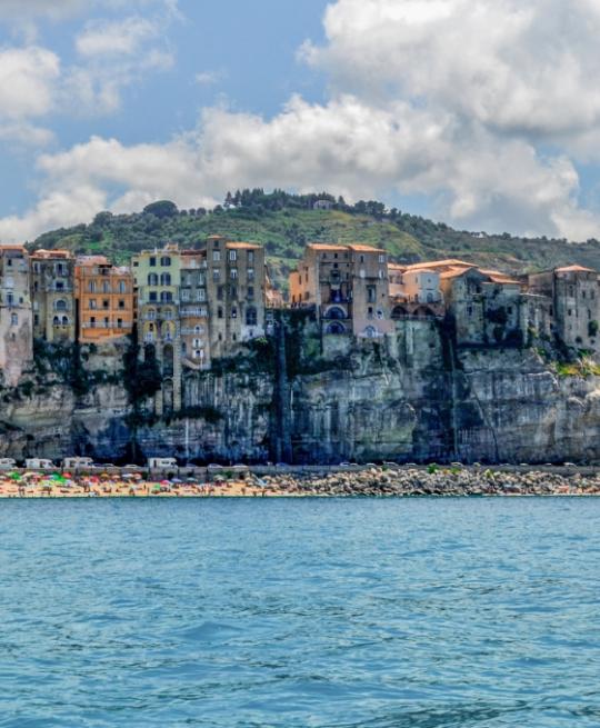 Case su una scogliera con spiaggia e mare, cielo nuvoloso.