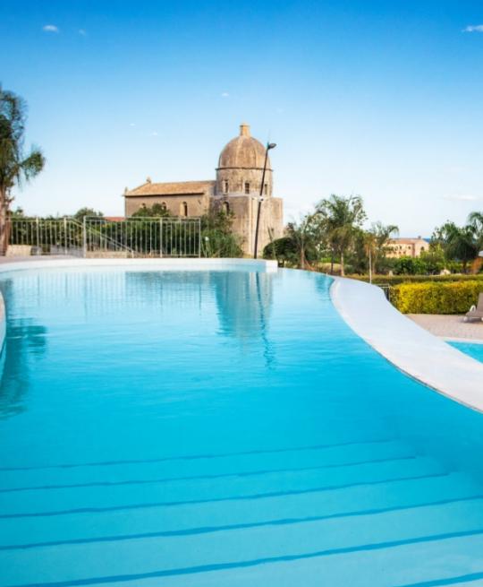 Piscina a sfioro con vista su un antico edificio e palme.