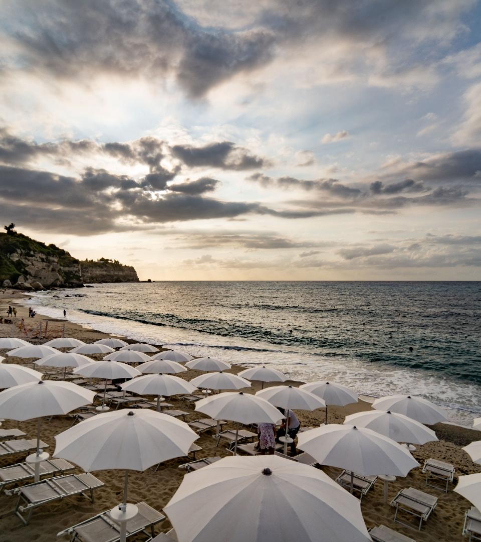 Spiaggia con ombrelloni bianchi al tramonto, mare calmo e cielo nuvoloso.